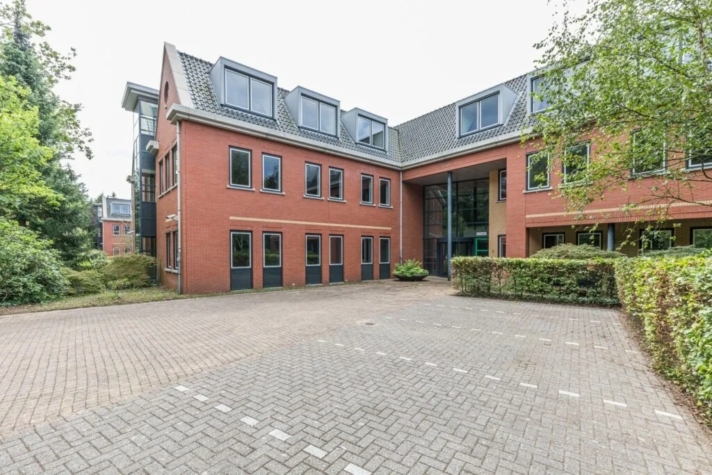 Kantoorgebouw aan de Laan Blussé van Oud-Alblas met rode bakstenen gevel, grote ramen en omliggende begroeiing.